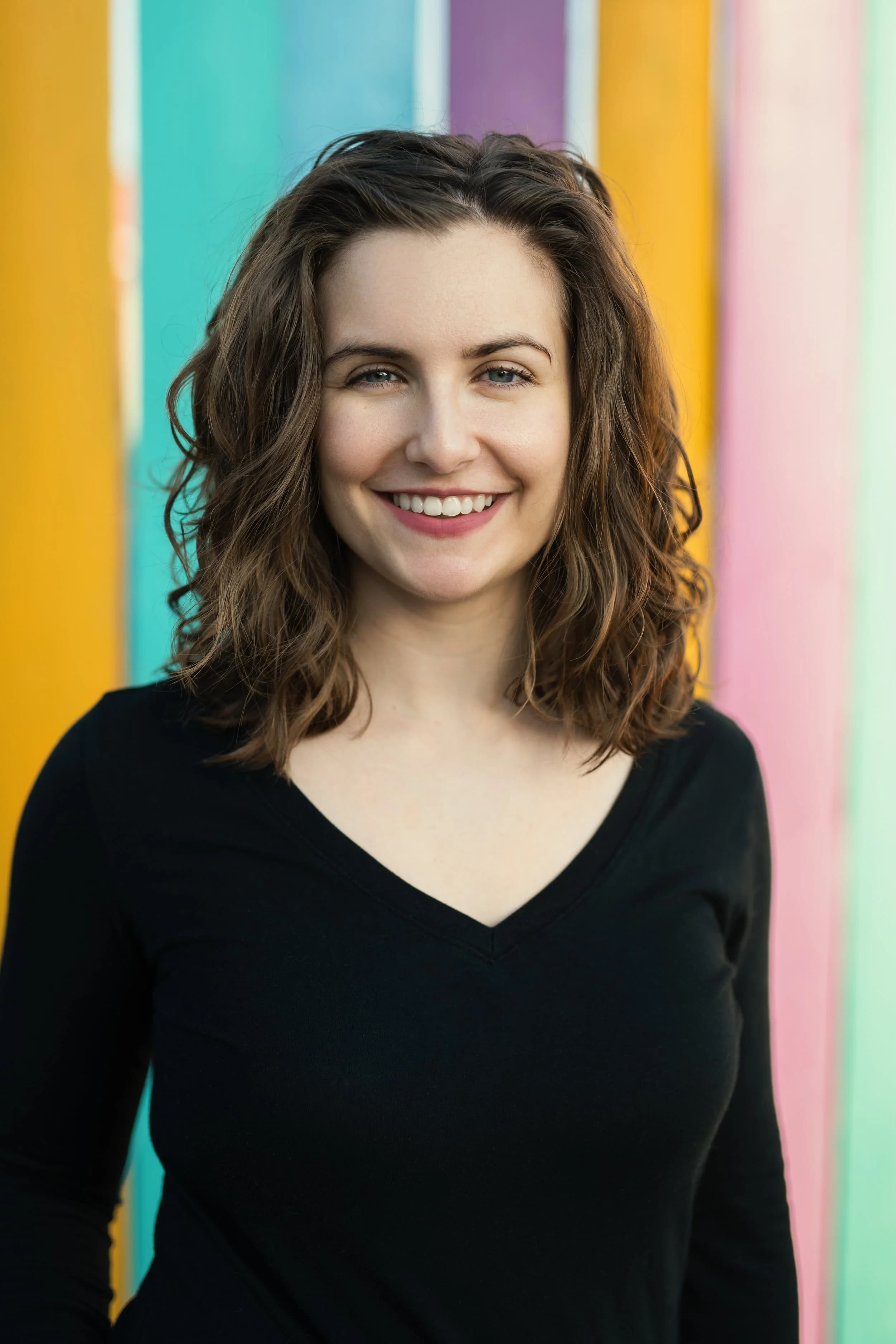 Dr. Renae DeLucia smiling in front of a wall painted in yellow, teal, purple, and pink stripes